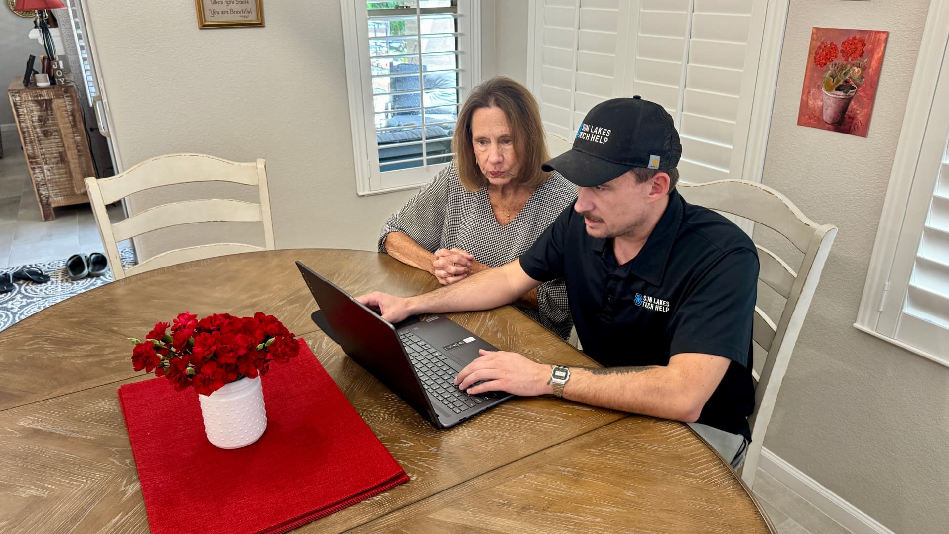 A Sun Lakes Tech Help technician working alongside a neighbor at her dining table